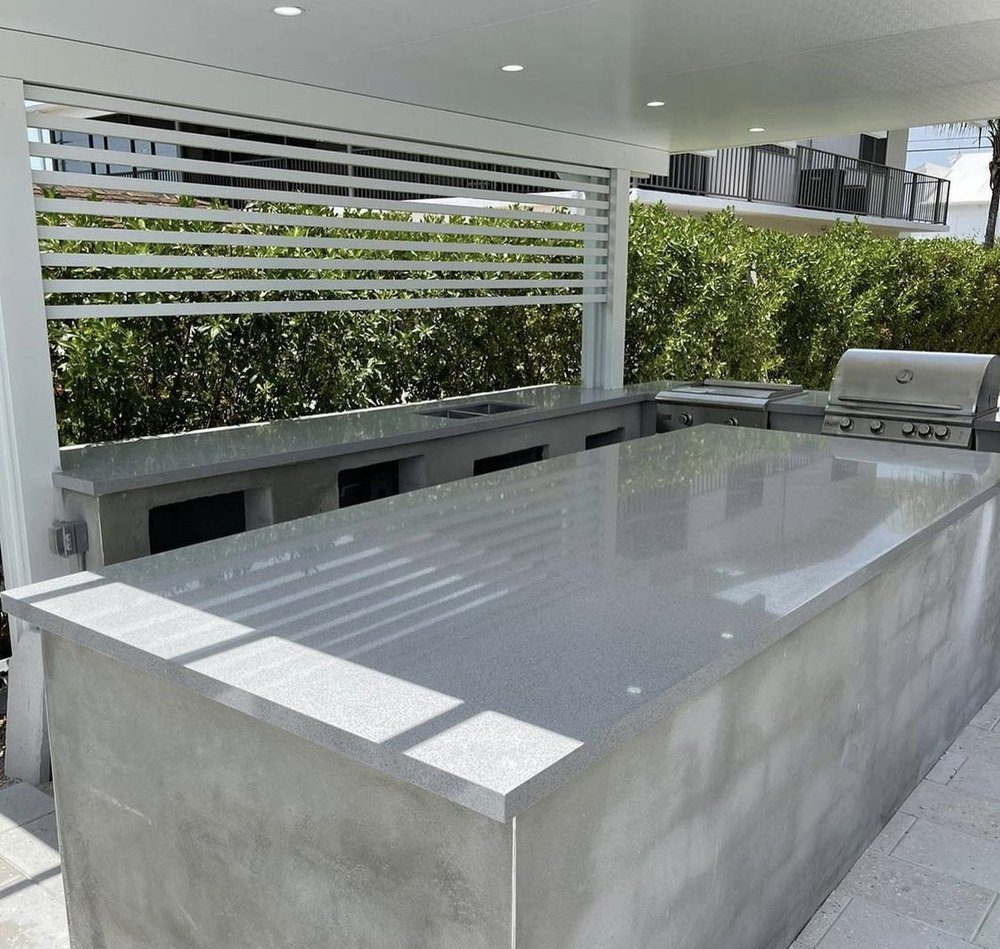 Outdoor kitchen with a grey quartz waterfall island and built-in grill